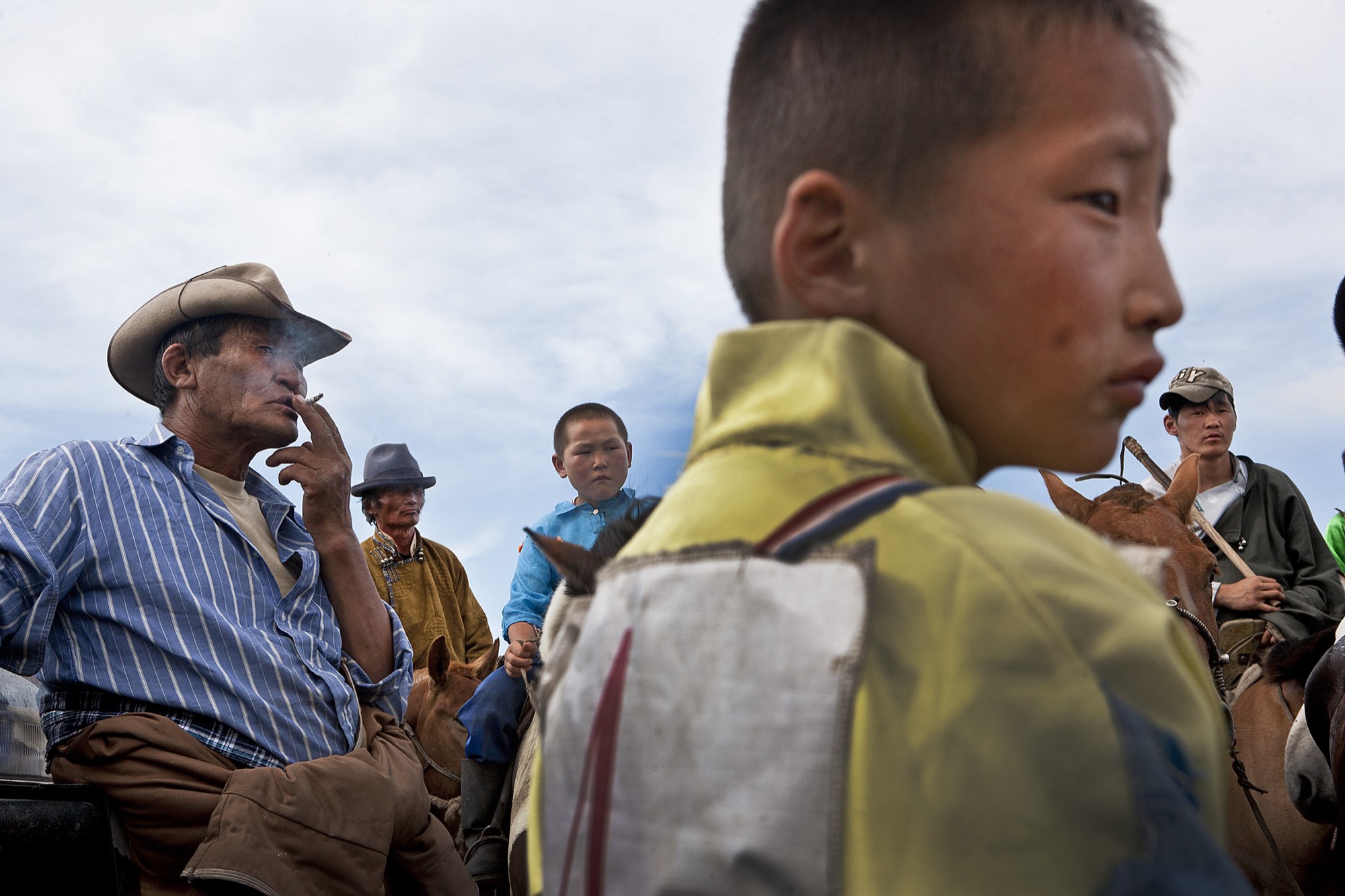 A young Mongolian boy in the foreground with herders gathered behind him